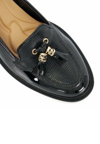 Zwarte loafers van textiel met een reptielenpatroon, gouden hardwareaccenten en zwarte kwastjes op de bovenkant. Textuurbodem.
