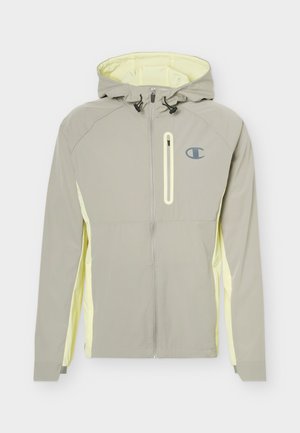 Helehall kapuutsiga jakk, millel on ees kogu pikkuses tõmblukk, rinnatasku tõmblukk, kontrastsed kahvatu kollased küljeosad ja sinine logo vasakul rinnal.