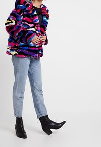 Multikleurige nepbontjas met een capuchon, voorzien van levendige strepen in roze, blauw en geel. Gecombineerd met lichtblauwe jeans en zwarte enkellaarsjes.