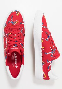 Rote Leinensneaker mit weißer Gummisohle, die ein verspieltes Baseballmuster aufweisen. Die Schnürsenkel und Akzente sind ebenfalls rot, mit einem Logo auf der Zunge.