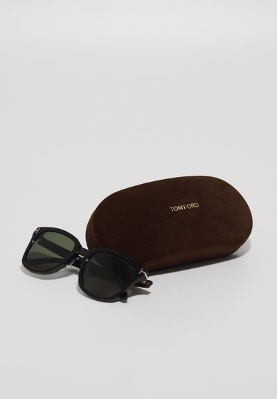 Tom Ford sunglasses with square black frames, dark lenses, and gold accents next to a brown suede case embossed with “TOM FORD.”