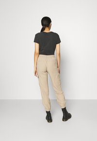 Dunkelgraues T-Shirt und beige Cargo-Hosen mit elastischen Bündchen. Schwarze Knöchelstiefel. Der Stoff wirkt weich mit einem lässigen Schnitt und praktischen Taschen.