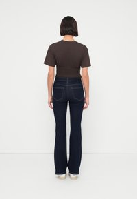 Σκούρο, εφαρμοστό τζιν με φαρδιά καμπάνα στο τελείωμα, συνδυασμένο με κοντομάνικο καφέ πουκάμισο cropped με σφηκοφωλιές στη μέση.