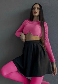 Maglietta rosa a maniche lunghe con orlo a scallop, abbinata a una gonna nera e collant rosa. Tessuti morbidi, design aderente e colori a contrasto.