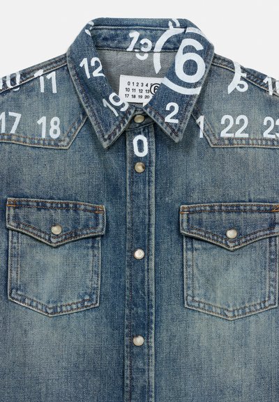 Τζιν μπουφάν με κουμπιά τύπου snap, δύο τσέπες στο στήθος και λευκούς αριθμούς τυπωμένους και διασκορπισμένους στο γιακά και τους ώμους.