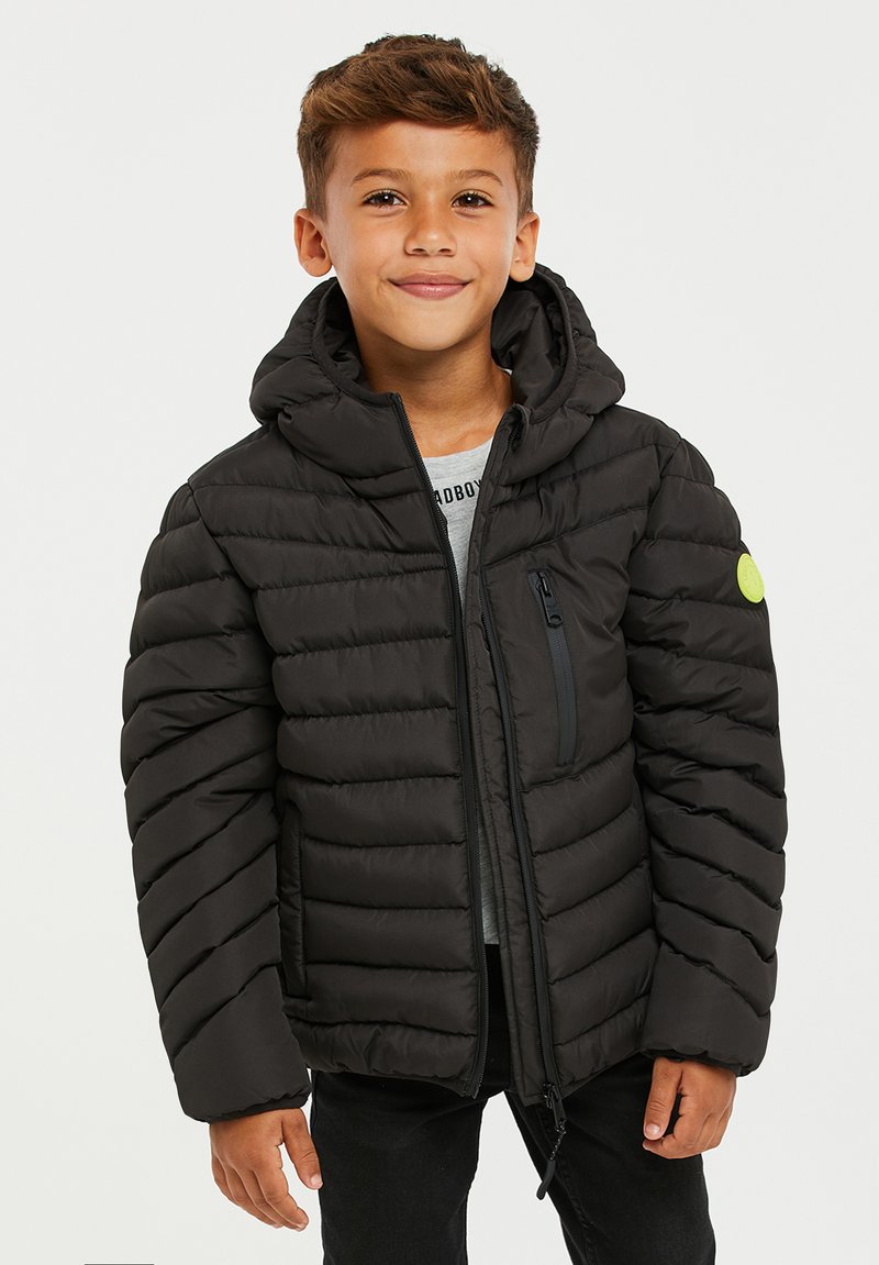 Chaqueta tipo puffer negra con cierre frontal, capucha y bolsillos laterales. Presenta paneles horizontales cosidos y un parche de logo verde en la manga.