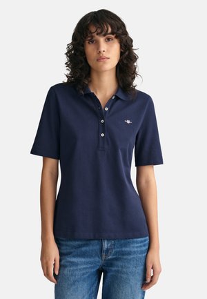 Polo bleu marine à manches courtes, avec col et patte à trois boutons. Présente un logo discret sur la poitrine et une texture en coton doux.