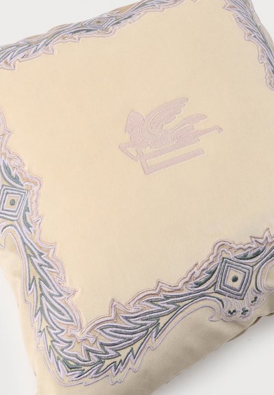 Coussin crème avec un emblème central de cheval ailé brodé et une bordure géométrique ornée dans des tons pastel.