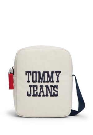 Maža balta stačiakampė pečių rankinė su tamsiai mėlynu dirželiu ir priekyje juodai siuvinėtais žodžiais „TOMMY JEANS“.