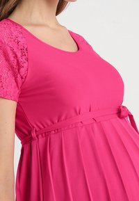 Fuchsiafarbenes Umstandskleid mit kurzen Spitzenärmeln, einem runden Ausschnitt und einem gebundenen Taillenband, mit einem plissierten Rock. Weicher, dehnbarer Stoff.