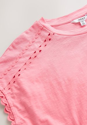 Roosa lühikeste varrukatega t-särk ümmarguse kaelusega, millel on lainelise servaga ja õmbluste kohal olevad lõhikdetailid. Materjaliks puuvill.