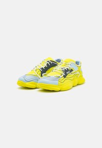 Sneakers with a blue and yellow design, featuring a textured upper, thick sole, curved lines, and white laces. Black accent on the side.