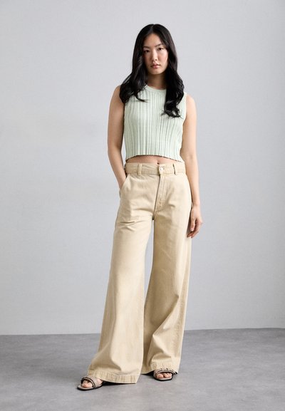 Un crop top côtelé vert clair associé à un pantalon large beige. Le pantalon présente une fermeture à bouton et des poches avant, en tissu léger.