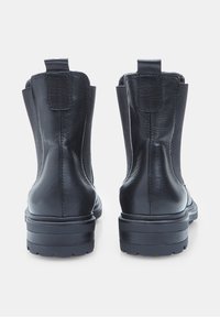 Fekete bőr bokacsizma pár, húzófülekkel és vastag talpú gumitalppal, hátulról egy fehér háttér előtt.