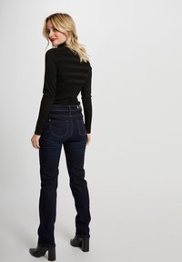 Zwarte geribbelde lange mouw top gecombineerd met donkerblauwe strakke jeans. De jeans hebben een hoge taille en een rechte pijpdesign met minimale hardware.