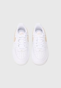 Valkoiset Nike Air Force 1 -tennarit kultaisilla yksityiskohdilla, joissa on sileä nahkapinta, nauhakiinnitys, pathologiset rei'itykset ja teksturoitu kumipohja.