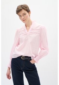 Lyserød bluse med v-hals, dekorative øjeindlæg og puffede ærmer. Sammen med mørke denimbukser og et sort bælte.