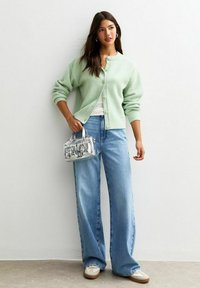 Cardigan a maglia verde menta, top bianco, jeans a gamba larga blu chiaro e una piccola borsa argentata. Scarpe casual con suola beige.