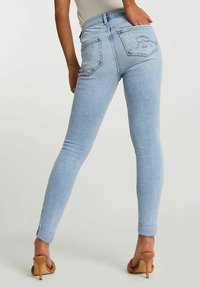 Los jeans ajustados de color azul claro presentan un diseño ceñido con una cintura alta, dobladillos enrollados y bolsillos traseros con detalles de costura.