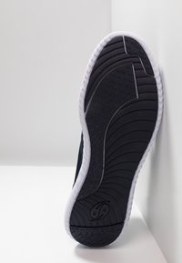 Sole di sneaker nera con bordo bianco, motivo di battistrada testurizzato, misura 43 contrassegnata, posizionata verticalmente contro muri d'angolo su superficie bianca.