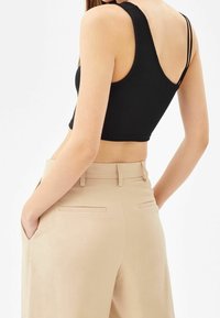 Černý žebrovaný cropped top s širokými ramínky, spárovaný se světle béžovými kalhotami na míru s zadními kapsami a hladkou texturou.