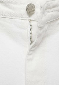 Tejido de mezclilla blanco con un zip plateado y botón de metal. La vista en primer plano muestra los detalles de la costura y la textura suave.