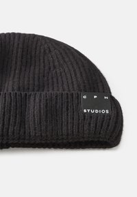 Black knit beanie with a fold-over cuff, featuring a square tag that reads "CPH STUDIOS" in white text. Textured ribbed pattern throughout.