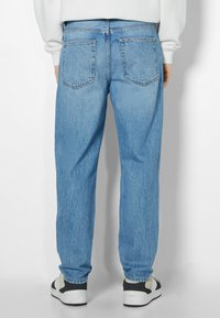 Vaqueros de mezclilla azul claro con un corte holgado, que presentan bolsillos traseros clásicos y un dobladillo limpio. Llevados con zapatillas negras y blancas.