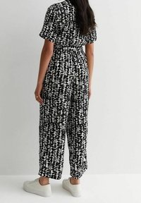 Monosuit de estampado en blanco y negro con mangas cortas, cinturilla elástica, piernas anchas y un ajuste relajado, combinado con zapatillas blancas.