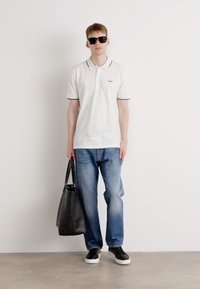 Polo bianco con dettagli blu navy, jeans azzurri, sneakers nere e una borsa a tracolla nera, indossato da una persona con occhiali da sole.