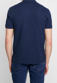 Námořnická polo košile s texturovanou tkaninou, krátkými rukávy a klasickým límcem. Zadní pohled ukazuje rovný lem bez vzorů.
