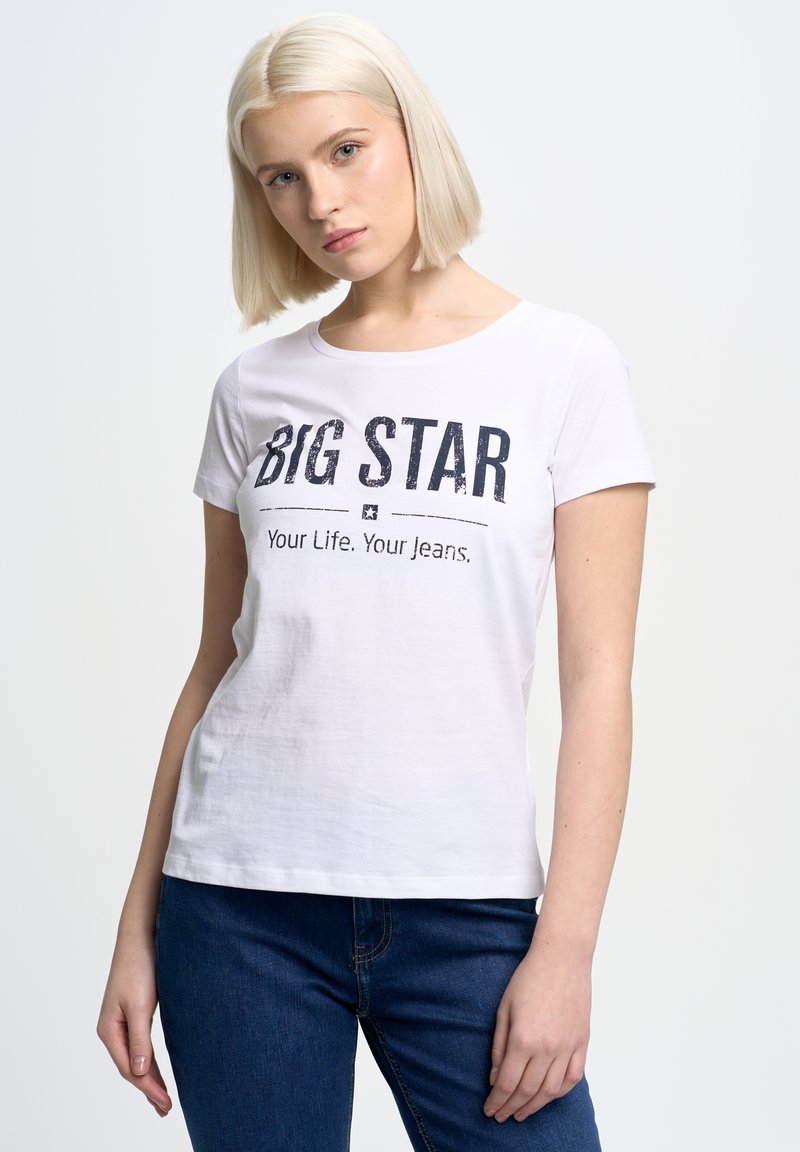 Bílý bavlněný tričko s potiskem "BIG STAR" v tmavém písmu. Krátké rukávy, kulatý výstřih a volný střih. V kombinaci s modrými džínovými kalhotami.