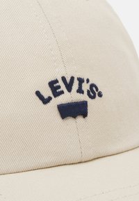 Cască de baseball din bumbac bej, având logo-ul brodat "LEVI's" în nuanță navy și o margine curbată semnată, cu detalii din țesătură texturată.