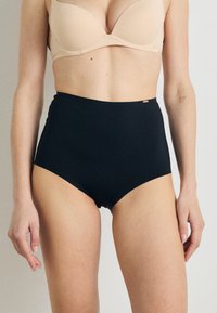 High-waisted black underwear made from smooth fabric, featuring a seamless design and a small metallic accent near the waistband.