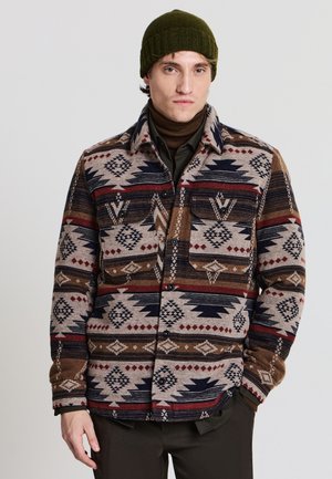 Veste chemise en mélange de laine avec un motif tribal aux teintes brun, marine et rouge. Deux poches poitrine, fermeture à boutons et un col avec une texture chaleureuse.