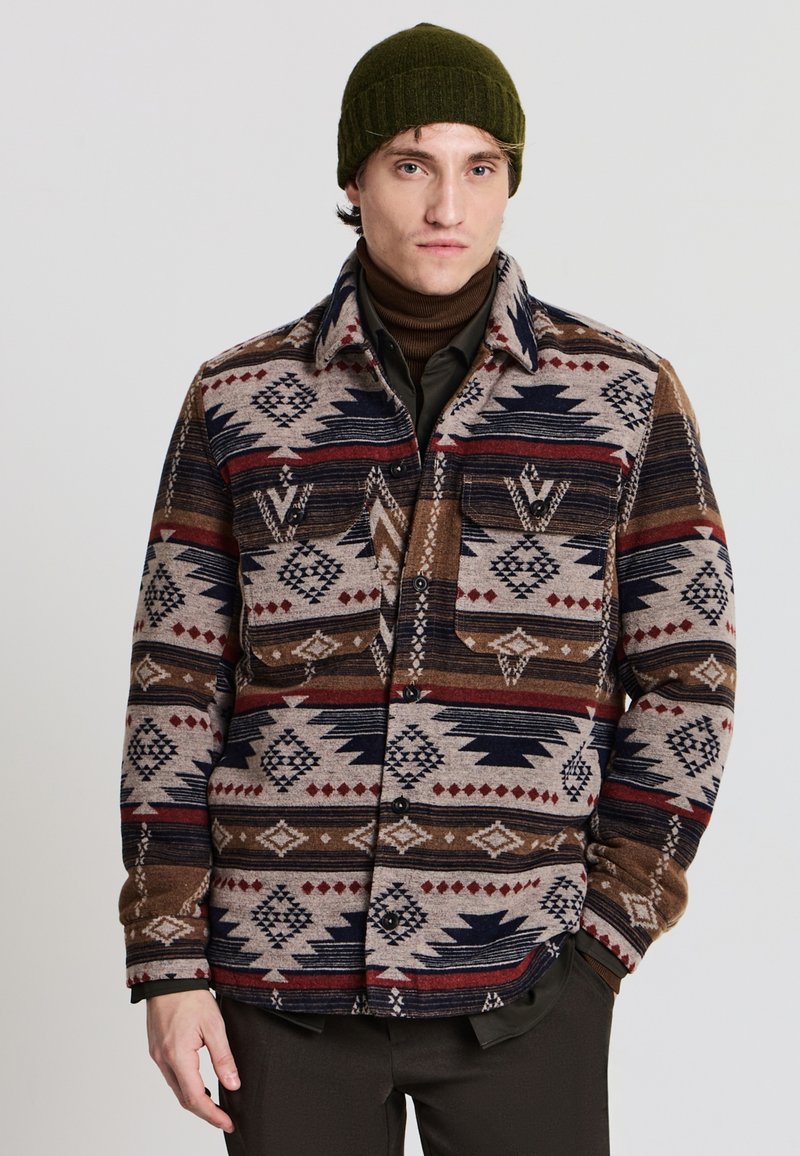 Hemdjacke aus Wollmischung mit einem Tribal-Muster in Braun, Marineblau und Rot. Zwei Brusttaschen, Knopfverschluss und ein Kragen mit warmer Textur.