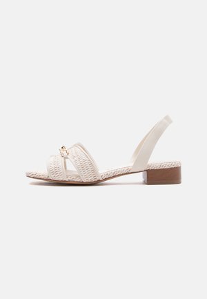 Witte gevlochten leren sandaal met lage hak, slingback bandje en een klein gouden kettingdetail op de voorste bandjes.