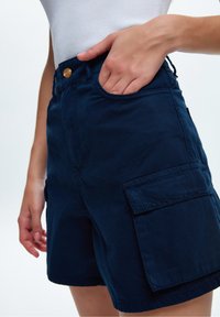 Pantalones cortos cargo de algodón azul marino con cierre frontal de botones y bolsillos laterales, que presentan una textura suave y un ajuste relajado.