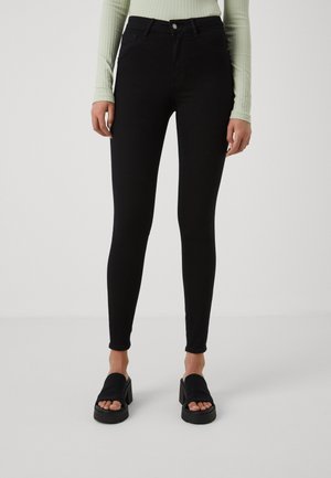 Sorte høyt liv jeans med en tettsittende design, glatt tekstur og subtil stretch. Kledd med kraftige svarte sandaler.