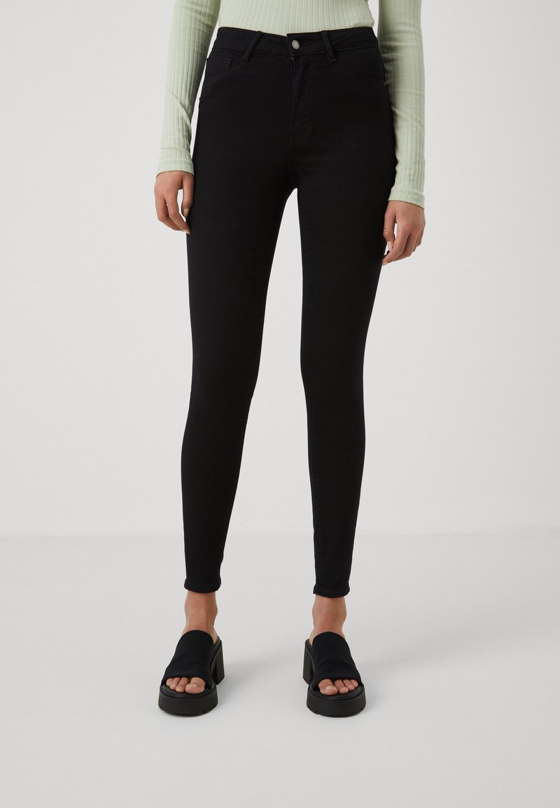 Black high-waisted jeans with a fitted design, smooth texture, and subtle stretch. Paired with chunky black slide sandals.