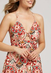 Robe à motifs floraux avec un design à décolleté en V, des bretelles réglables et un détail de nœud central en trou de serrure. Les couleurs incluent le rouge, le rose et le marron.