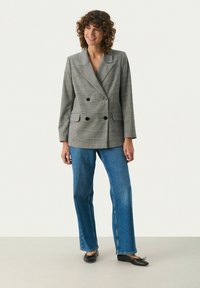 Grauer karierter doppelreihiger Blazer mit Revers, zwei Fronttaschen und schwarzen Knöpfen, kombiniert mit blauen Schlagjeans und schwarzen Ballerinas.