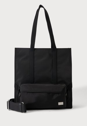 Sac fourre-tout rectangulaire noir avec longues poignées, une poche avant zippée et une bandoulière amovible sur fond blanc.