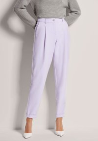 Lilac tailored trousers with front pleats, featuring a single button closure, cuffed hems, paired with white pointed-toe heels.