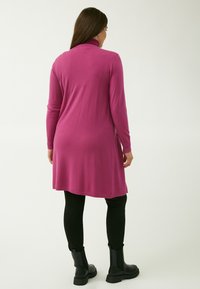 Abito a maniche lunghe in tessuto rosa solido con colletto alto. Abbinato a leggings neri e stivaletti. Tessuto morbido e vestibilità comoda.