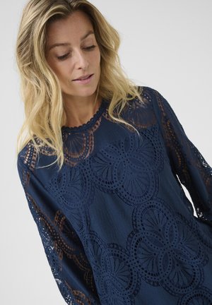 Marinblus med intrikata spetsdetaljer och blommönster. Långa ärmar med spetsaccent och rund halsringning. Mjuk textur.