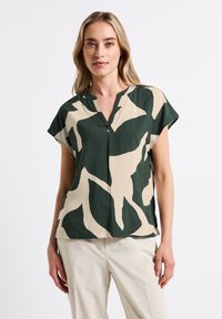 Blusa a maniche corte e scollo a V in tessuto verde e beige con un motivo astratto. Materiale leggero con una vestibilità rilassata.