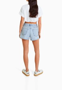 Ljusblå denimshorts med hög midja, bakfickor och fransad fåll, kombinerat med en kort ärmad vit t-shirt och vita sneakers.