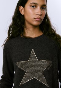 Suéter de punto gris oscuro con un gran diseño de estrella adornado con cuentas metálicas y costuras texturizadas, escote redondo y mangas raglán.