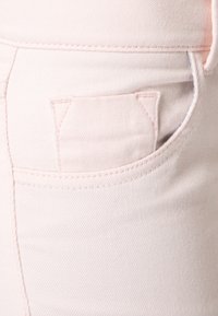 Ljusrosa denimtyg har en liten, sned bakficka med rena sömmar. Texturen verkar jämn och något stretchig.